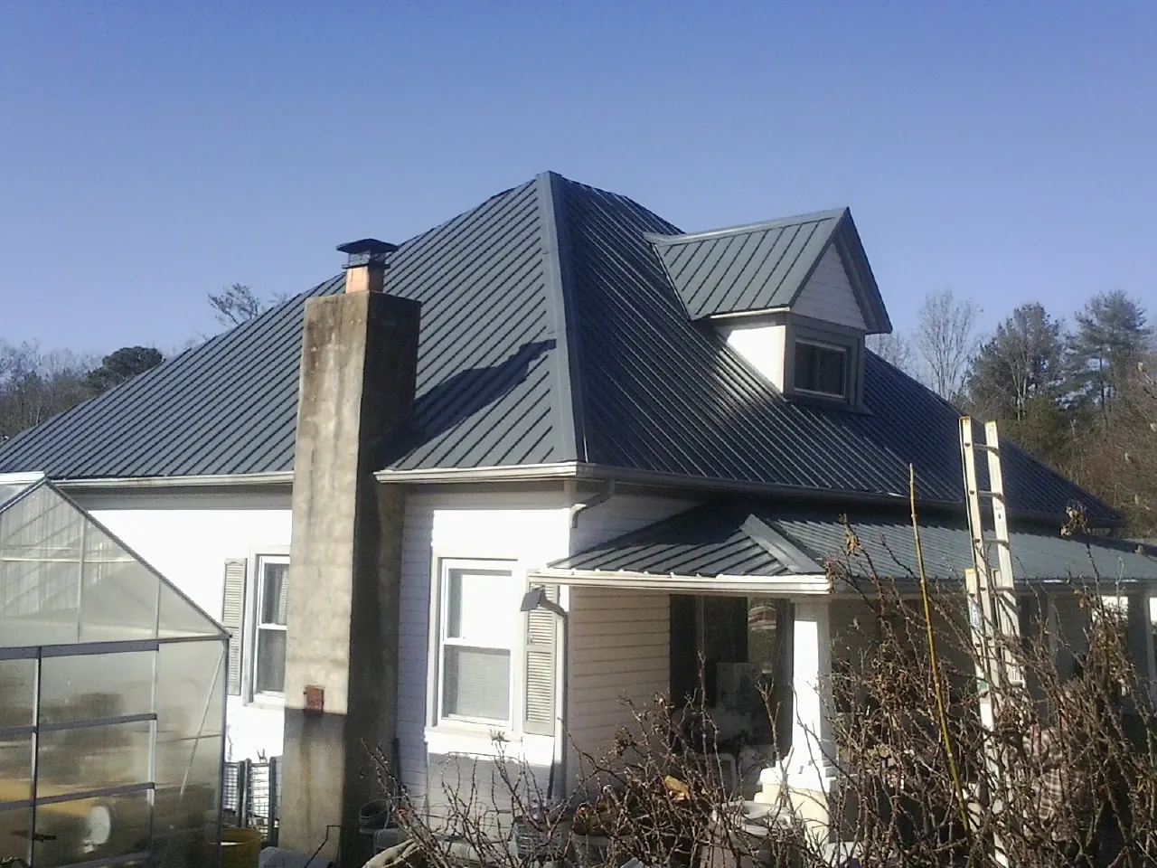 Dark blue standing seam metal roof on a white farmhouse with dormer — Slate & Tile Roof Repair by Roofing Brothers in Smelterville