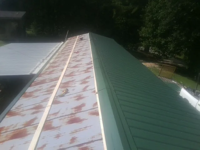 Old rusted panels beside newly installed green metal roofing — Wind Damage Roof Repair by Roofing Brothers in Smelterville