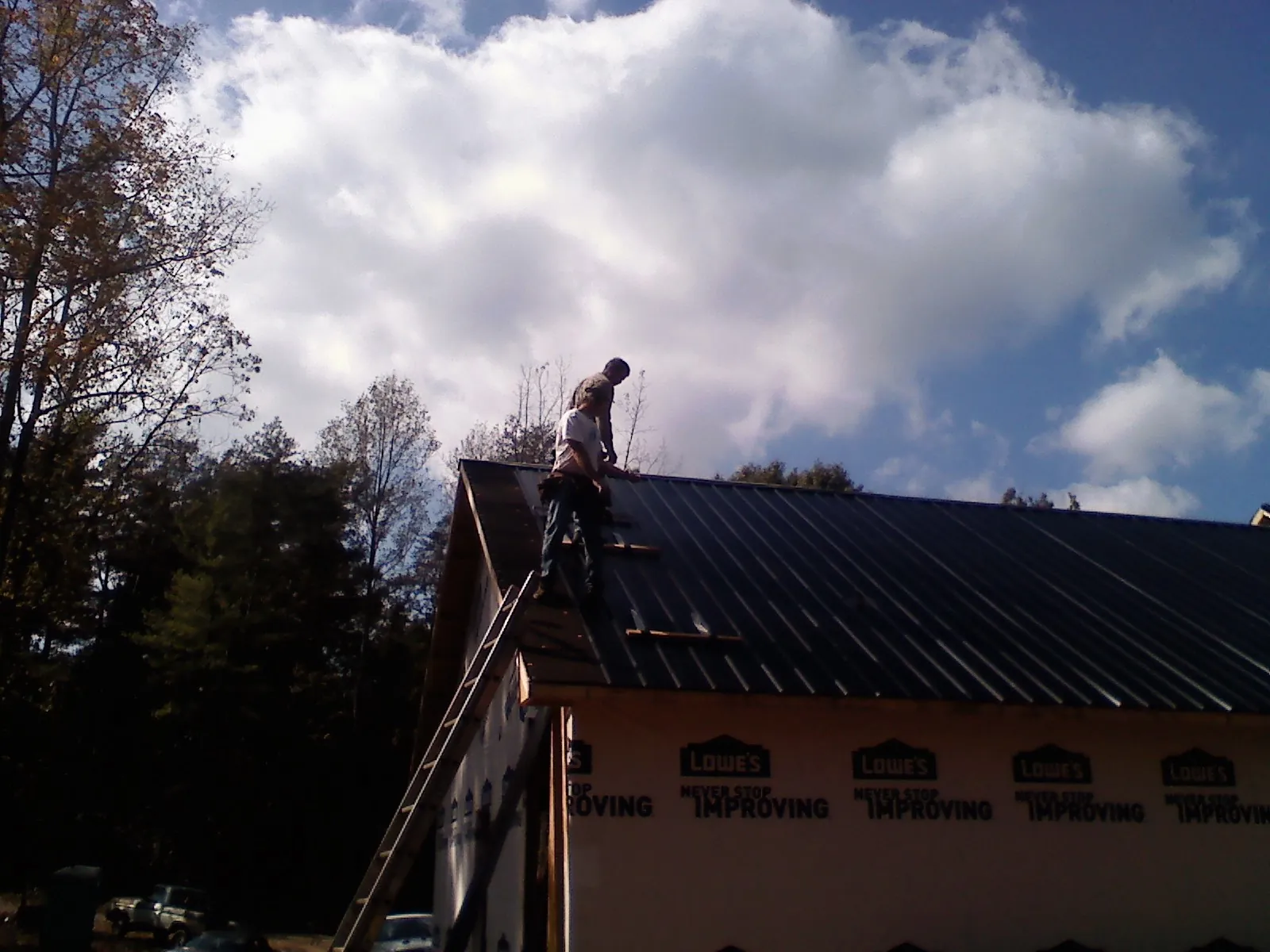 Roofer fastening dark metal panels high against a cloudy sky, from a Roof Inspection job in Smelterville