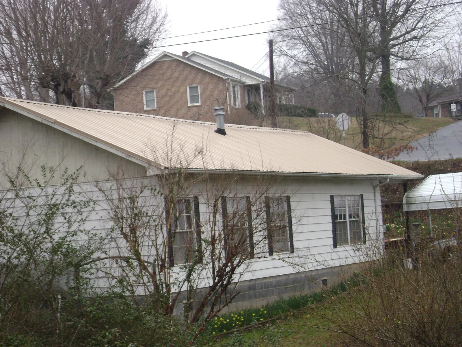 Tan metal roof on a white sided house set into a hillside — Commercial Roofing by Roofing Brothers in Smelterville
